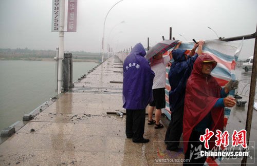 图为大风吹垮的桥栏已被清理，工人们在冒雨加装围挡。